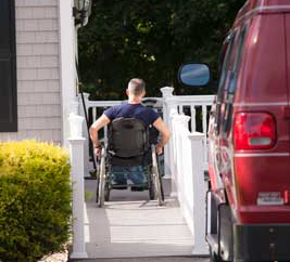 a photo of a man using a wheelchair to go up his ramp to his home